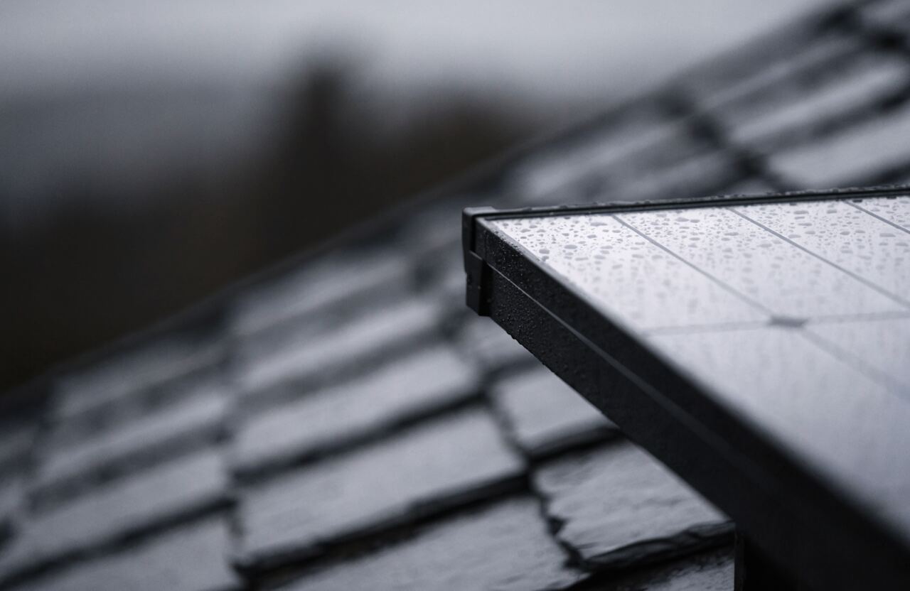 Close-up of an all-black solar panel on a slate roof with raindrops on the glass